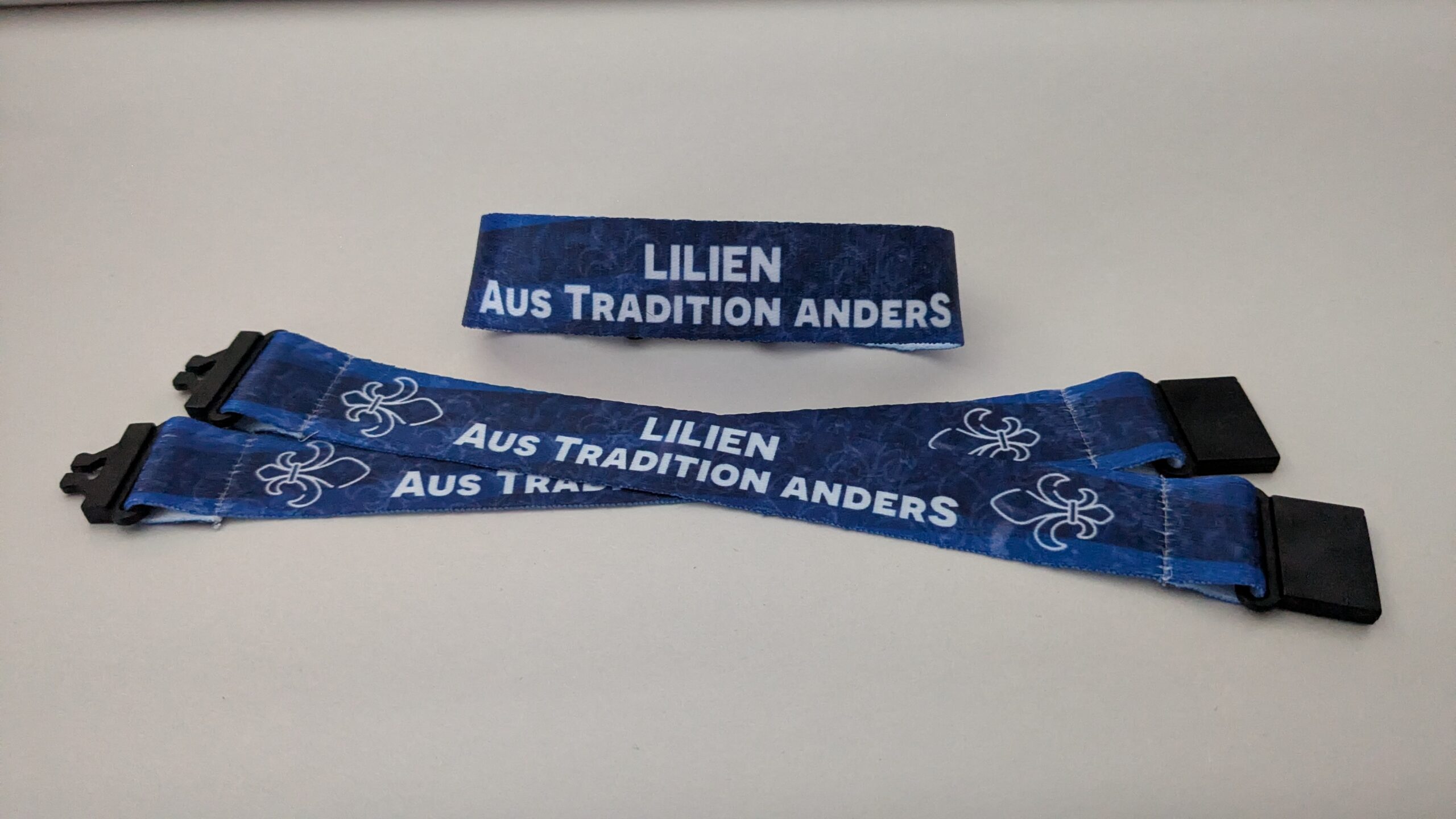 Armband in verschiedenen Blautönen mit dem Text "Lilien - Aus Tradition anders" in weiß.